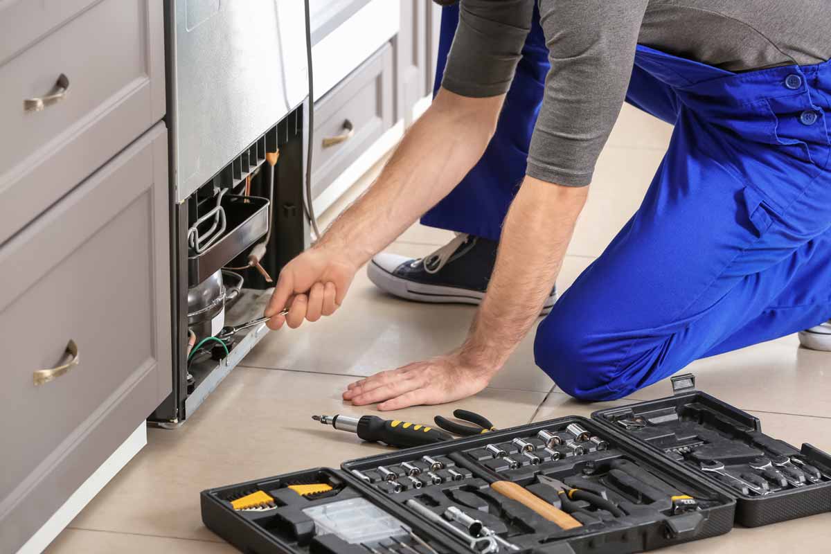 An appliance repair technician repairing the wiring on the bottom of a refrigerator