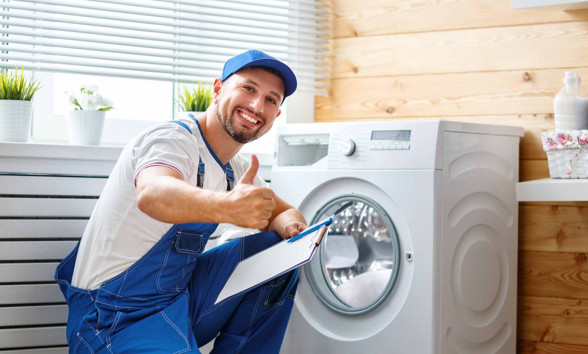 Appliance repair technician posing in front of a washer/dryer and giving a "thumbs up" gesture